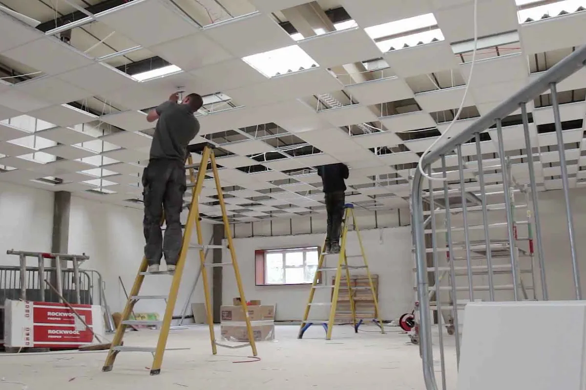 Office fit-out in progress — commercial electrician installing suspended ceiling lighting